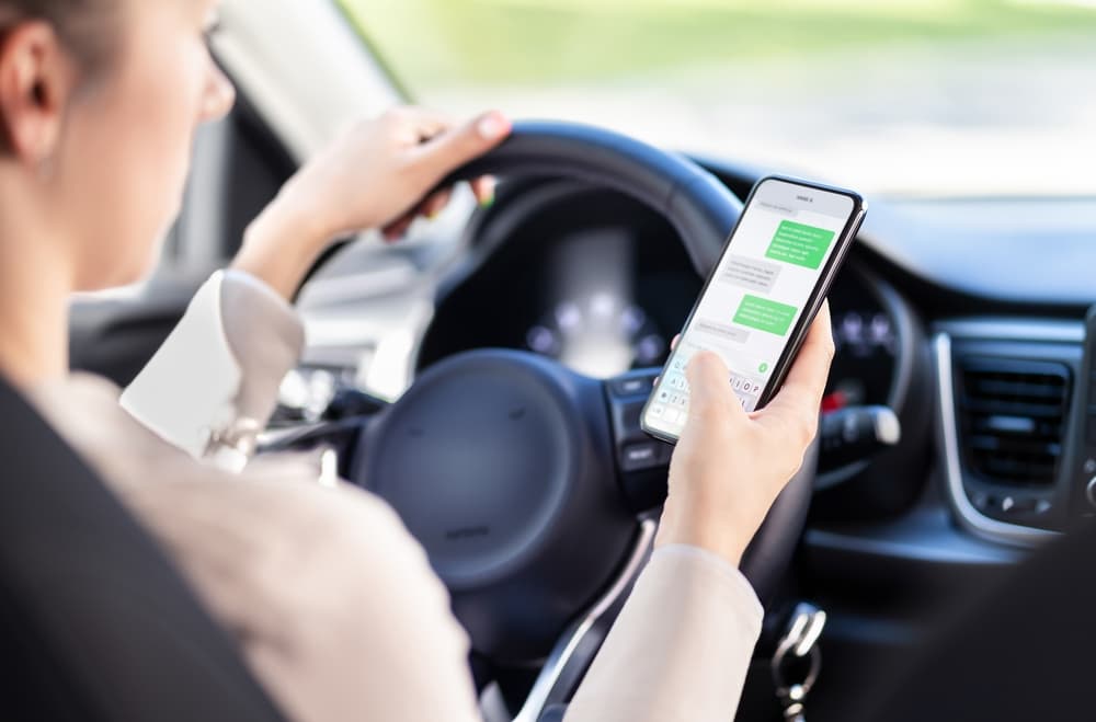 Distracted driver using a phone while driving. Woman texting on her mobile device in traffic, highlighting unsafe behavior and the risk of auto accidents.